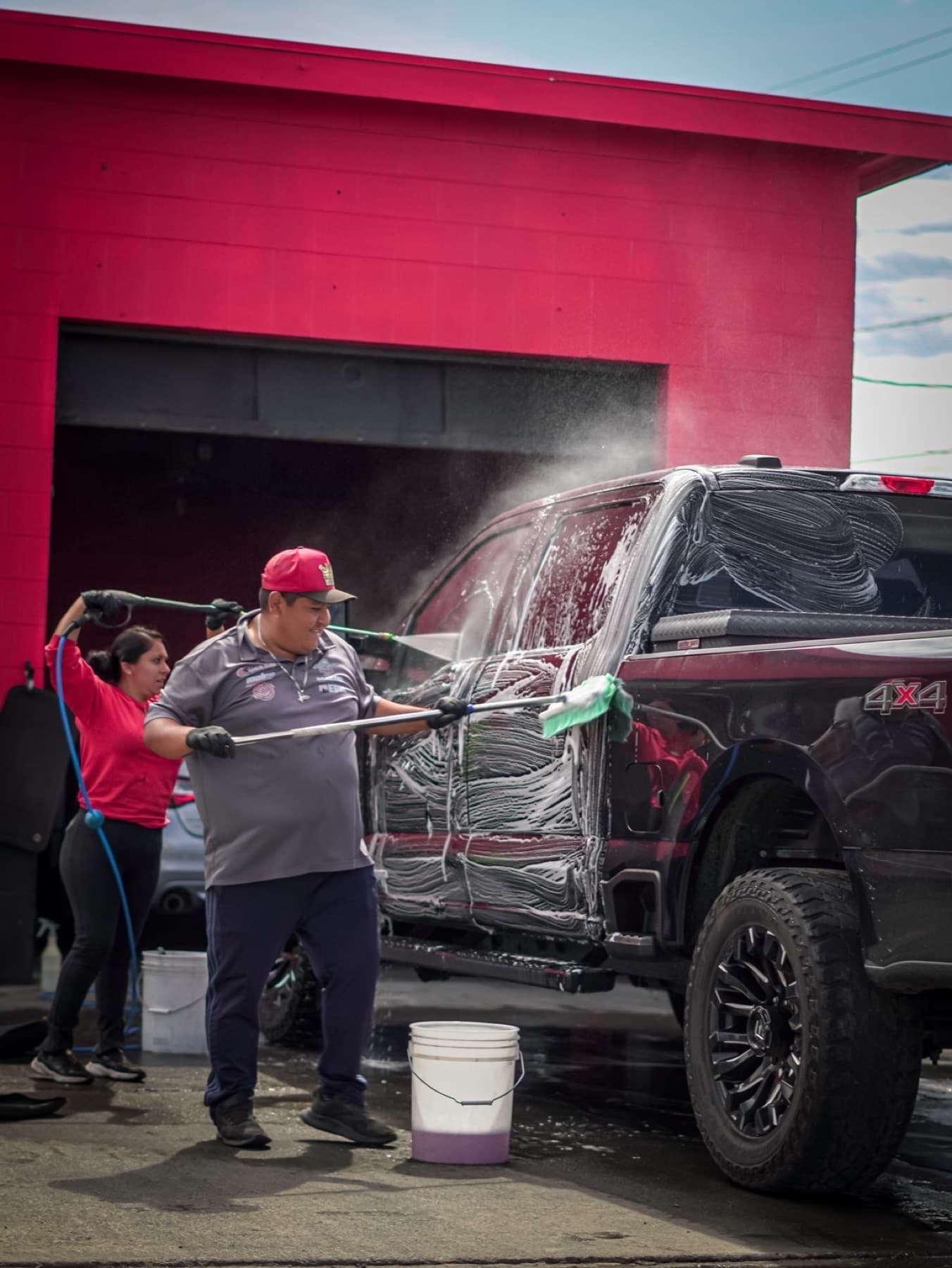 King Detail washing a black truck with foam outside a red detail bay.